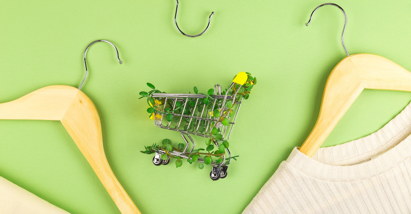 Shopping cart with leaves in it surrounded by clothes on a green background