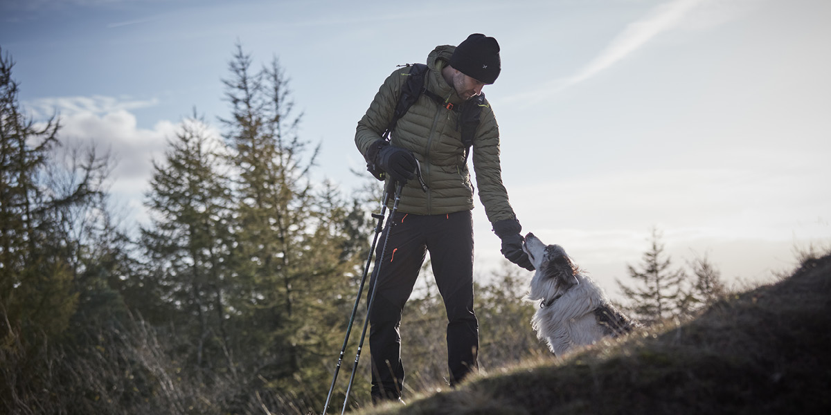 Man petting dog on a hill side with walking gear
