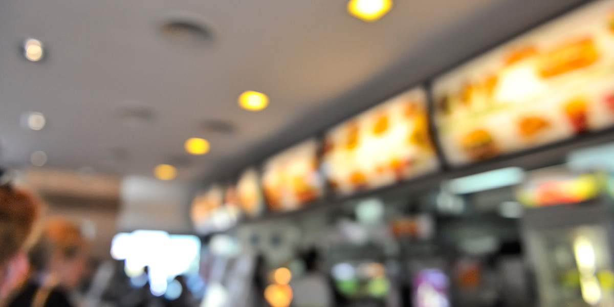 Blurred image of fast food restaurant with digital menu screens at ordering counter