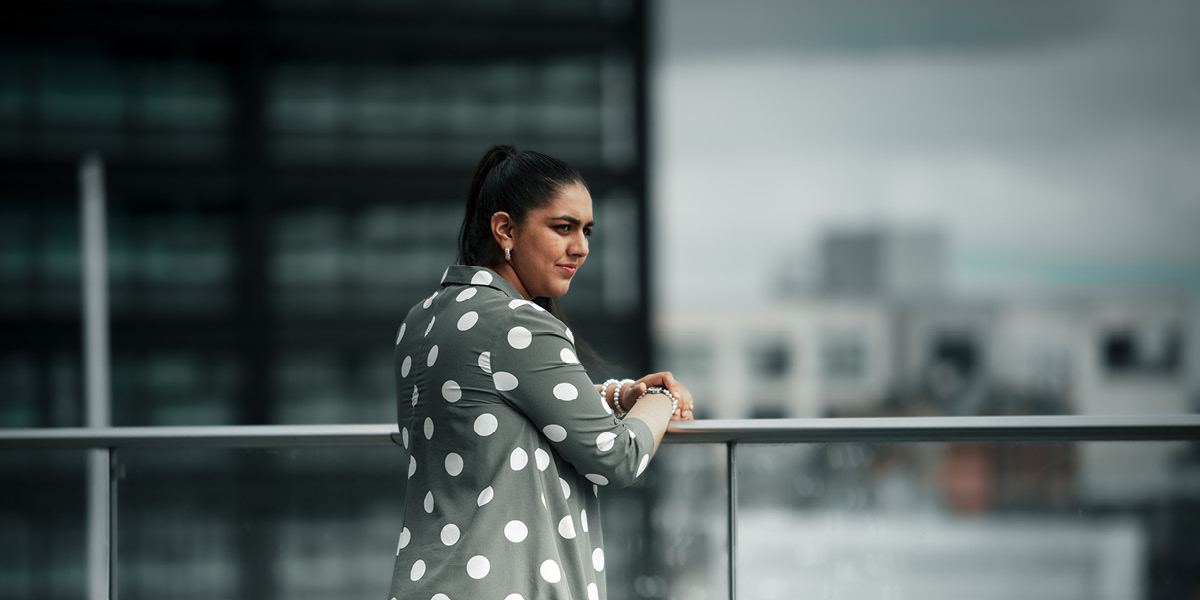 Lady standing against a railing looking out into the distance with a cityscape background