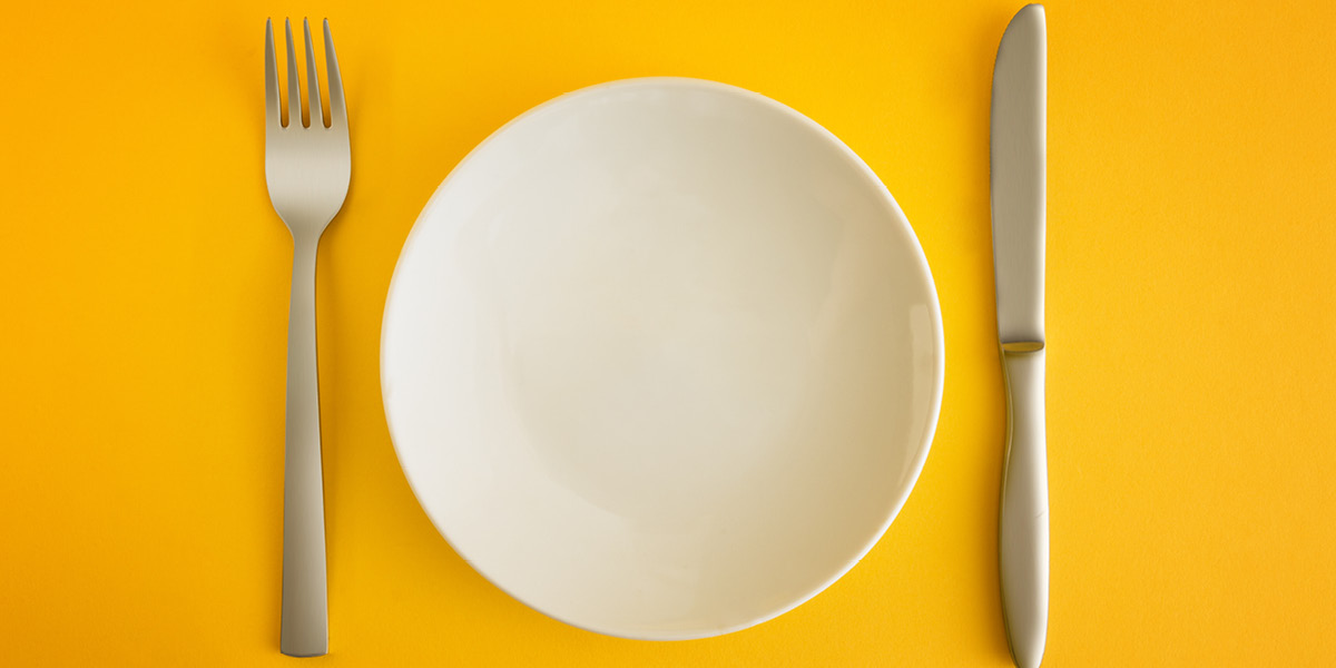 Dinner plate, knife and fork set against a yellow background