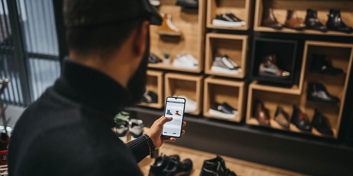 Man shopping on phone whilst looking at shoes in store