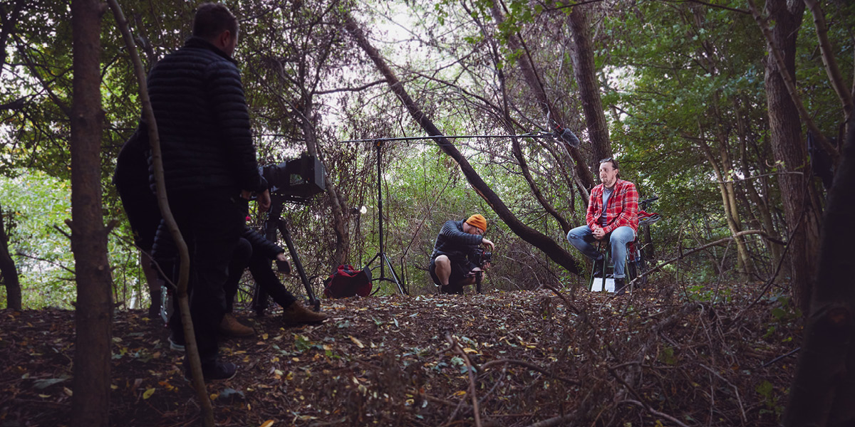 Camera crew in a forest filming documentary film with young person sitting in the middle