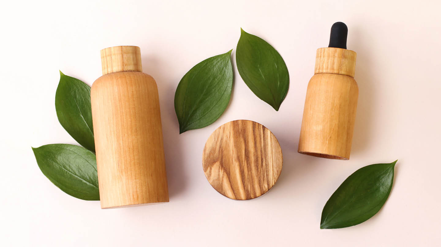 Wooden cosmetic bottles laid on top of leaves on a white background