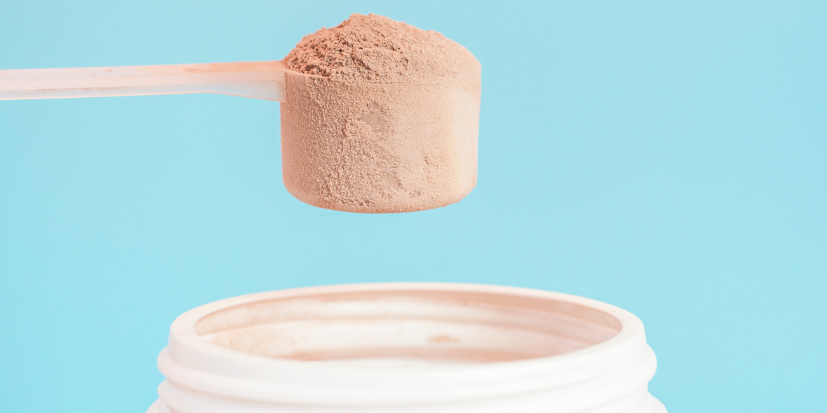 scoop full of protein powder above container on blue background