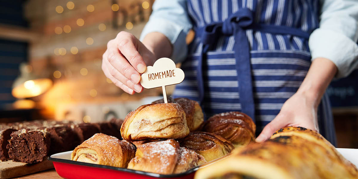 Person in a bakery with baked goods sticking a homemade sign in some cakes